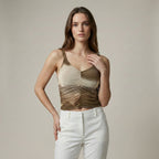 Woman wearing a gold tank top and white pants against a neutral background