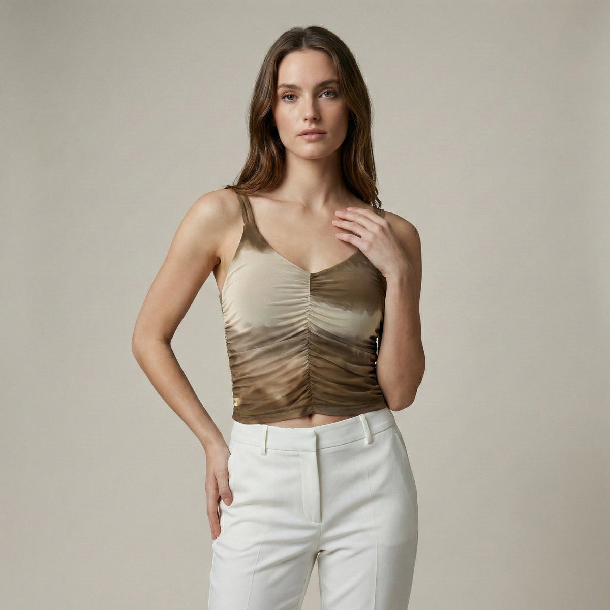Woman wearing a gold tank top and white pants against a neutral background