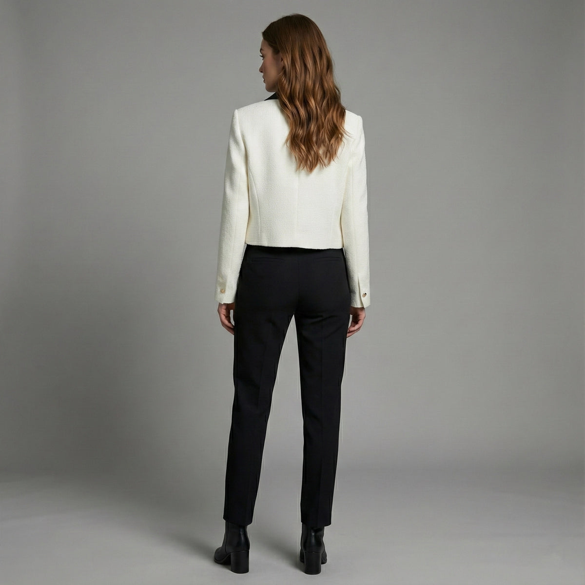 Woman wearing a white blazer and black pants against a gray background