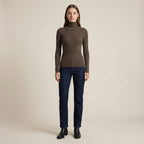 Woman wearing a brown turtleneck sweater and dark blue jeans on a beige background