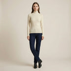 Woman wearing a beige turtleneck sweater and dark jeans on a plain background