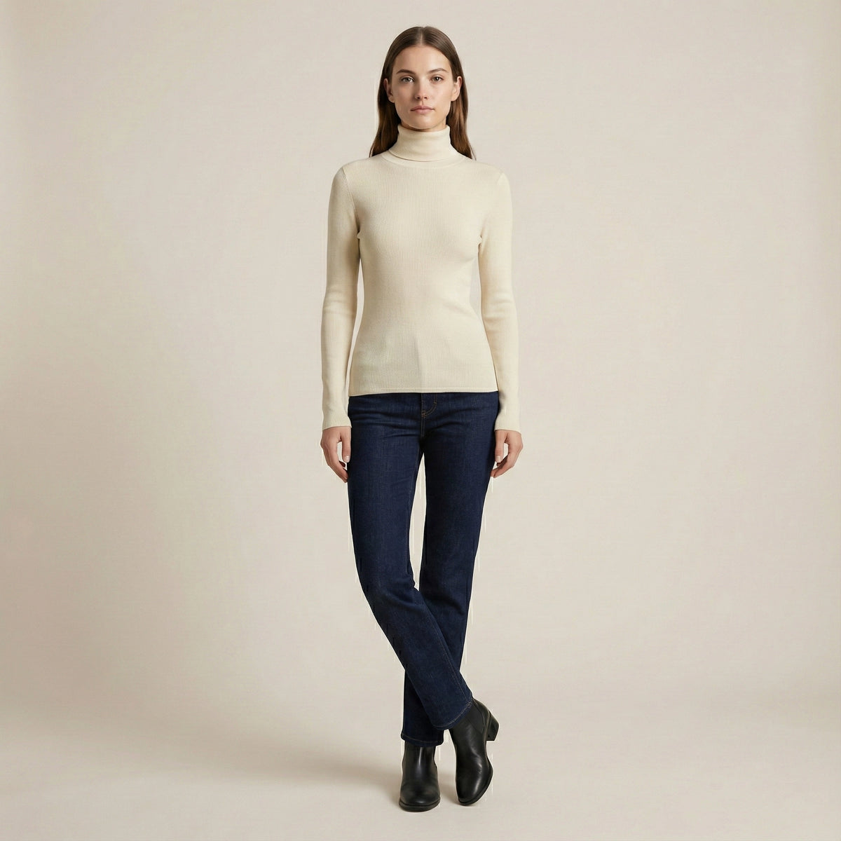 Woman wearing a beige turtleneck sweater and dark jeans on a plain background