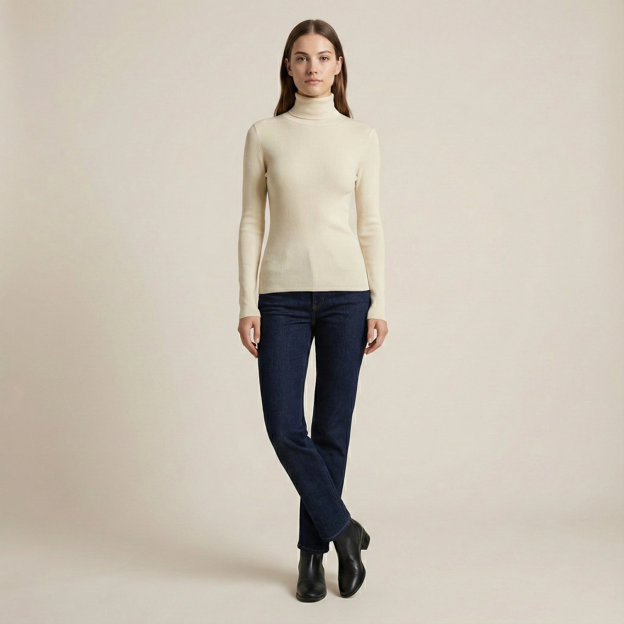 Woman wearing a beige turtleneck sweater and dark jeans on a plain background