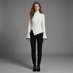 Woman wearing a white turtleneck sweater and black pants against a gray background