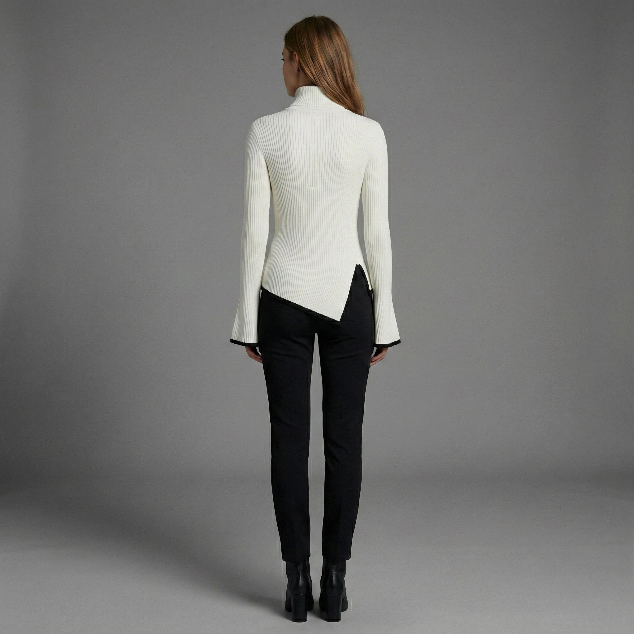 Woman wearing a white ribbed sweater and black pants against a gray background