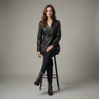 Woman wearing a black leather jacket and pants sitting on a stool against a plain background