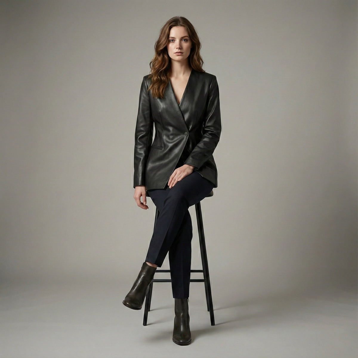 Woman wearing a black leather jacket and pants sitting on a stool against a plain background