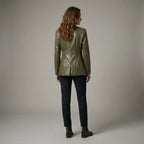 Woman wearing a green jacket and dark pants against a plain background