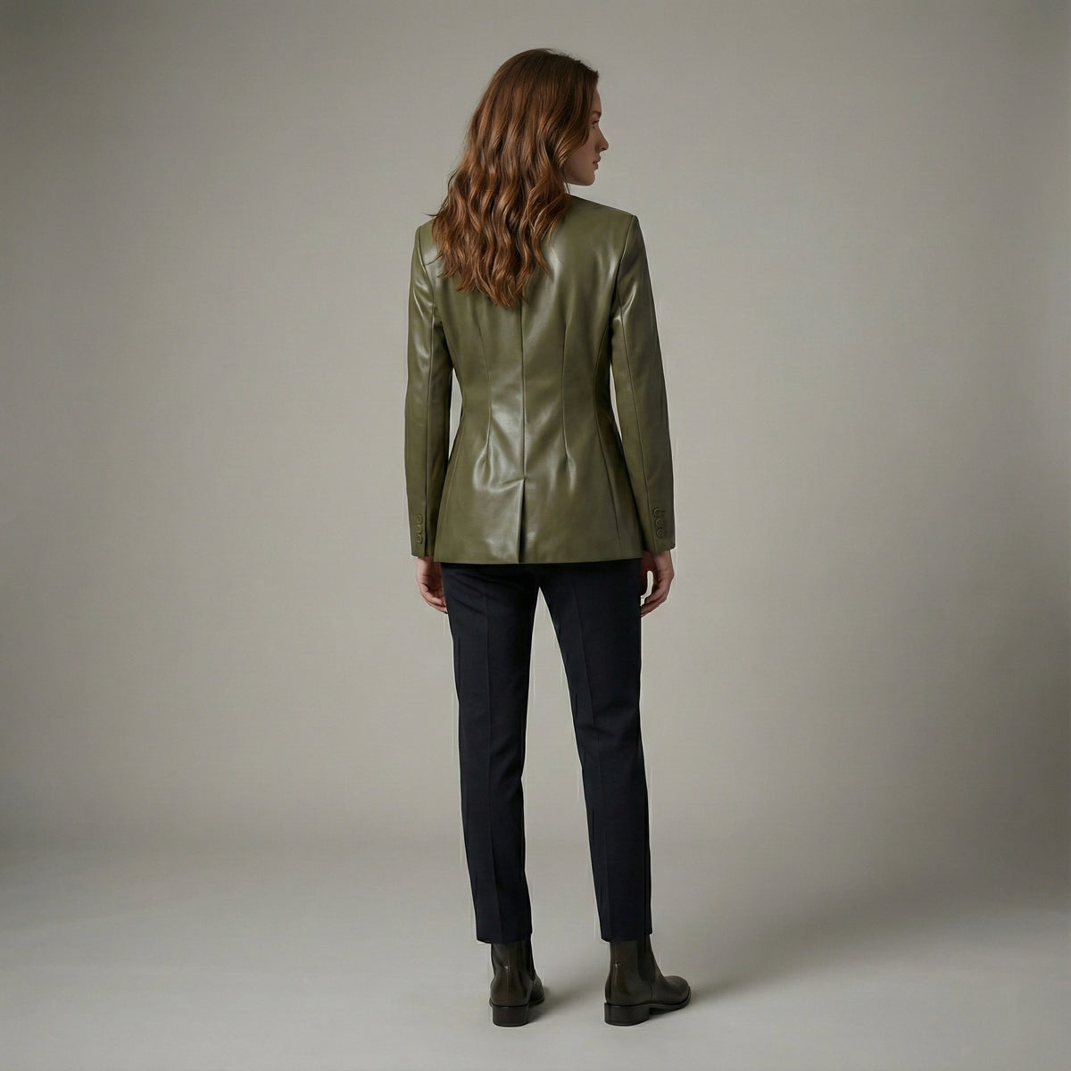 Woman wearing a green jacket and dark pants against a plain background