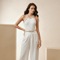 Woman wearing a white jumpsuit with gold accents in a neutral setting