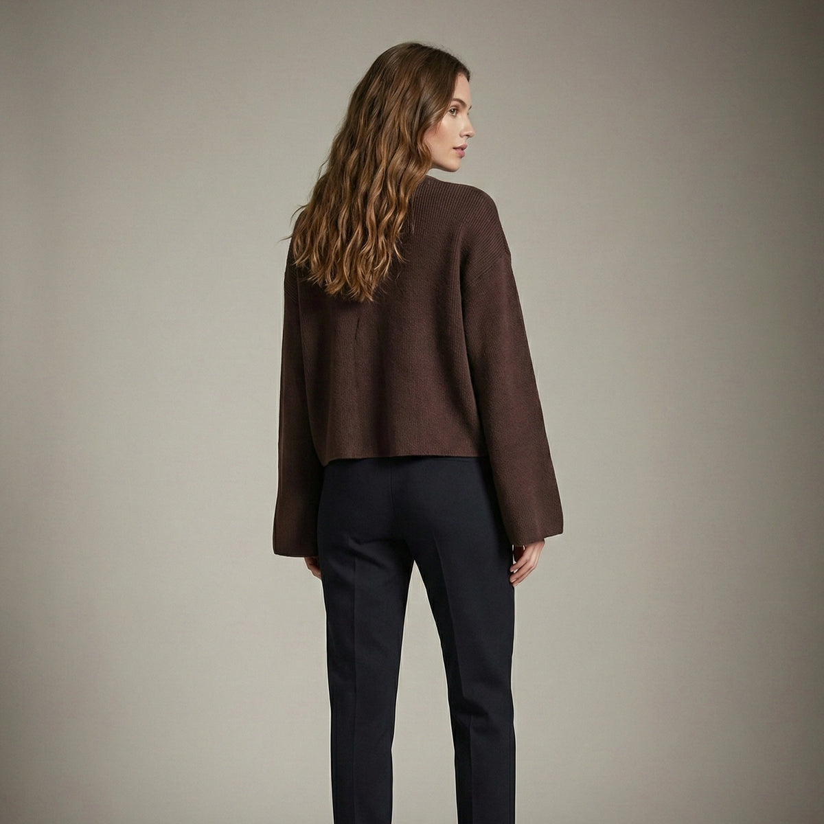 Woman wearing a brown jacket and black pants against a plain background