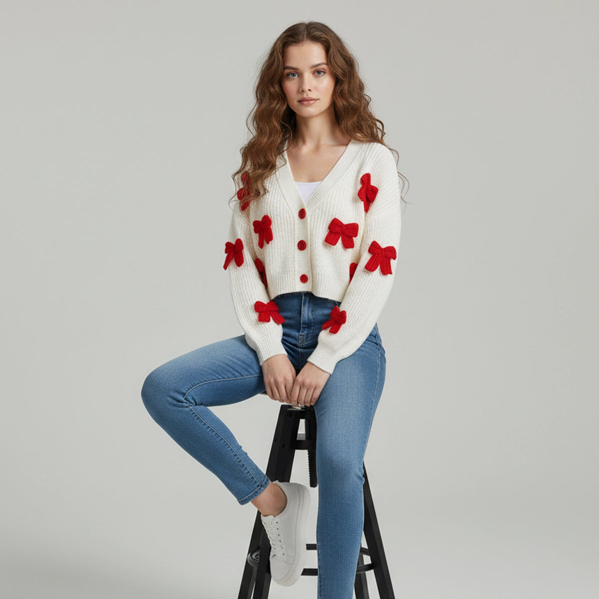 Woman wearing a white cardigan with red floral patterns and blue jeans on a gray background