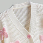 White knitted cardigan with pink buttons and trim on a light gray background