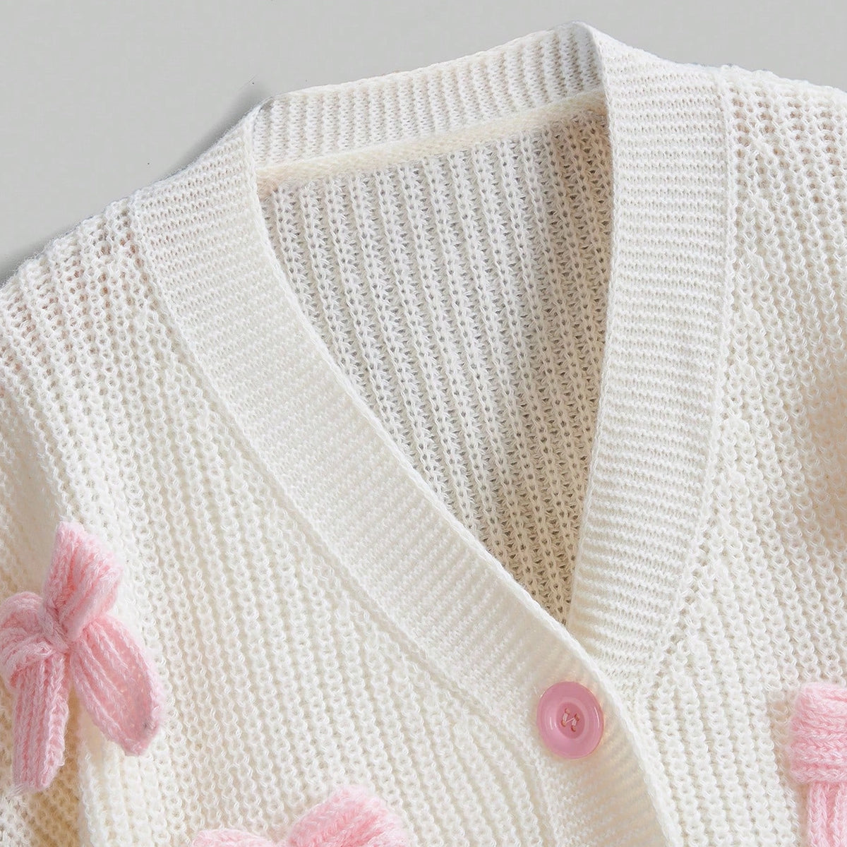 White knitted cardigan with pink buttons and trim on a light gray background