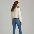Woman wearing a cream sweater and blue jeans on a gray background