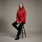 Person wearing a red jacket sitting on a stool against a plain background
