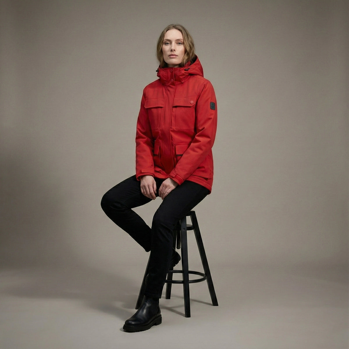 Person wearing a red jacket sitting on a stool against a plain background