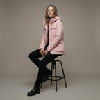Person wearing a pink jacket sitting on a black stool against a neutral background