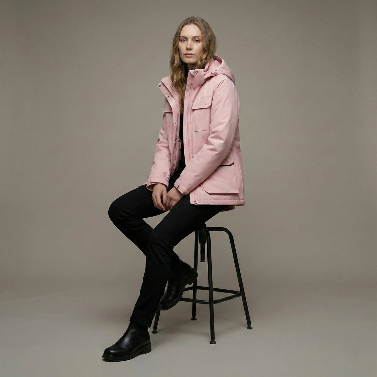Person wearing a pink jacket sitting on a black stool against a neutral background