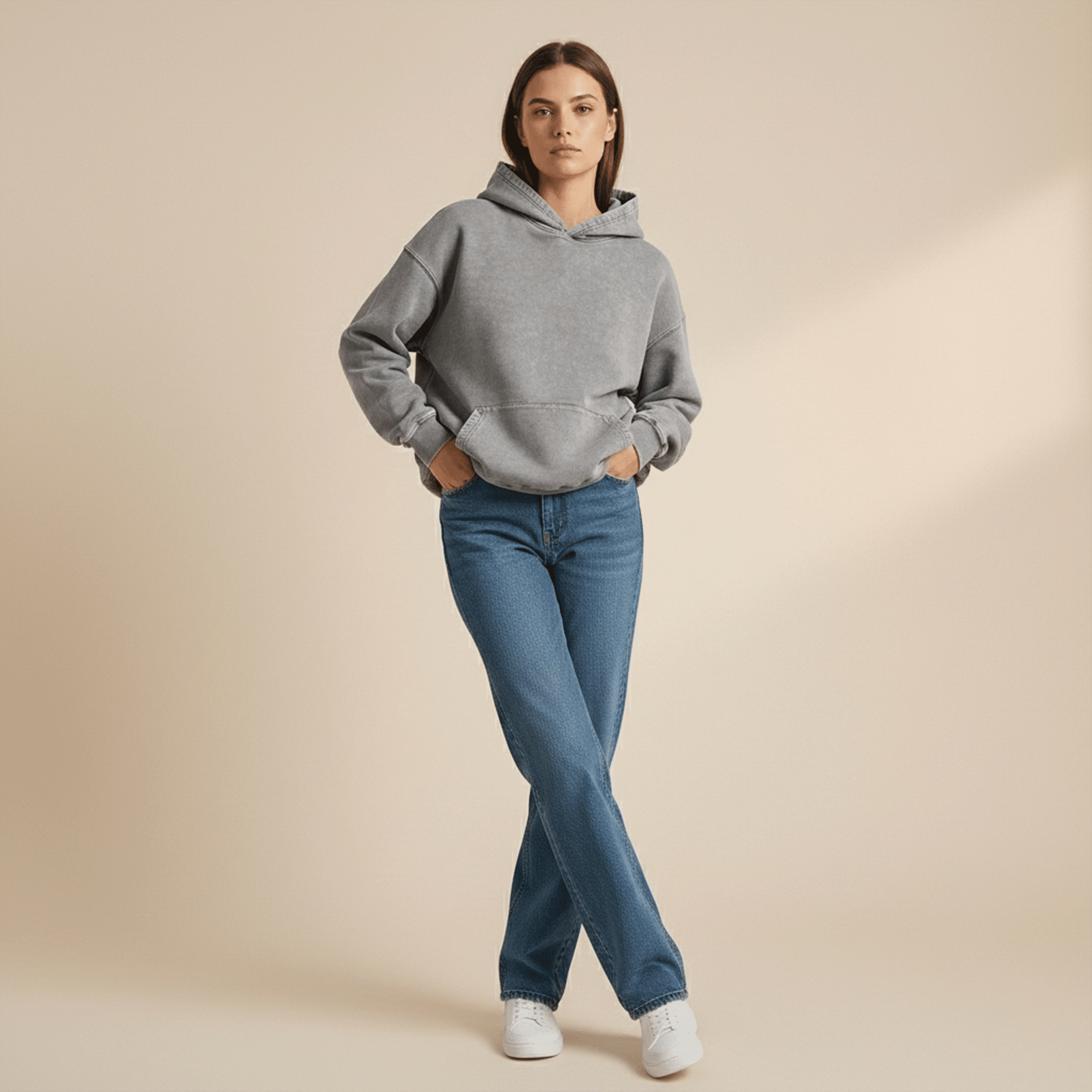 Woman wearing a gray hoodie and blue jeans on a beige background