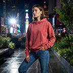 Woman wearing a red hoodie and blue jeans standing in a city at night with illuminated billboards in the background.