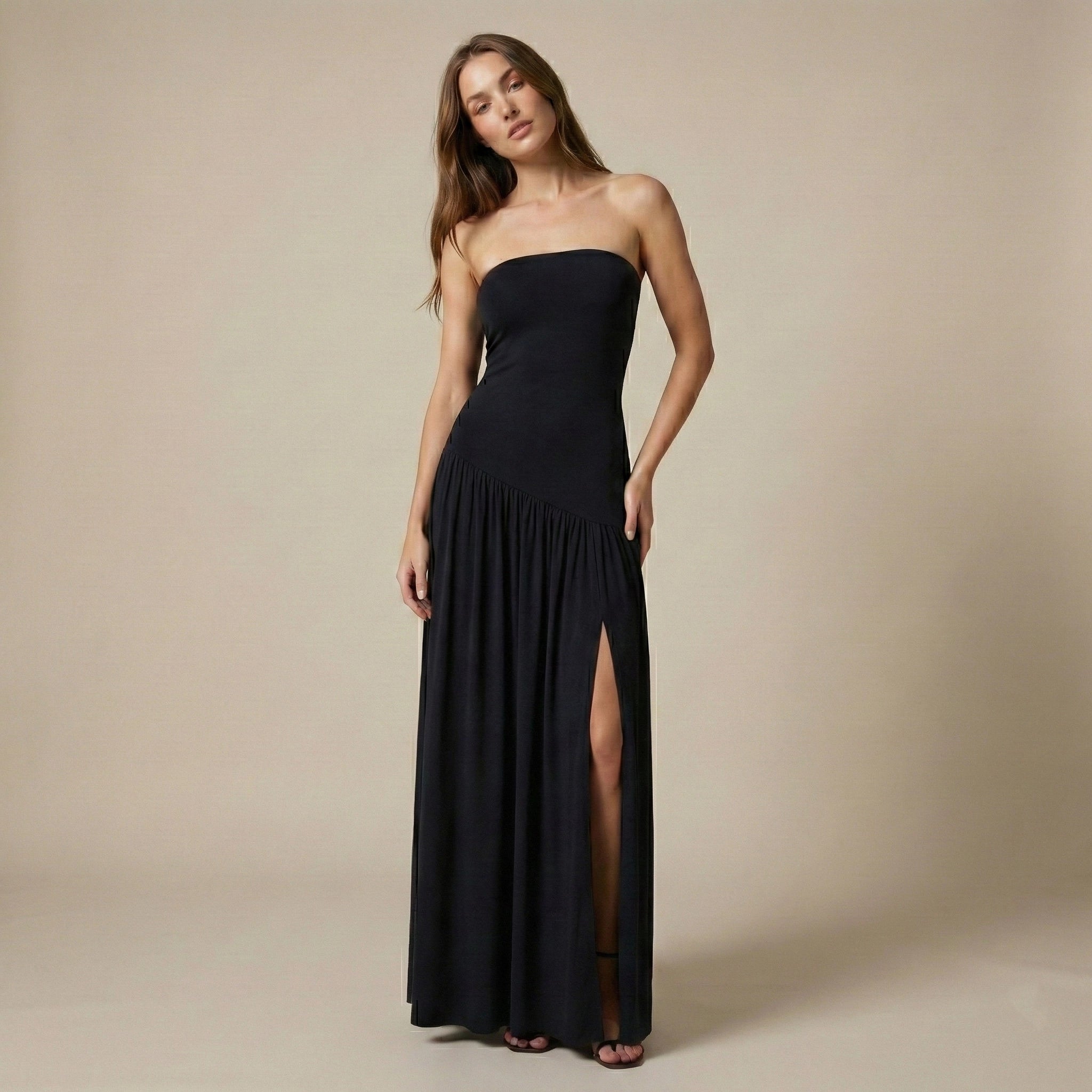 Woman wearing a black strapless gown with a slit on a beige background