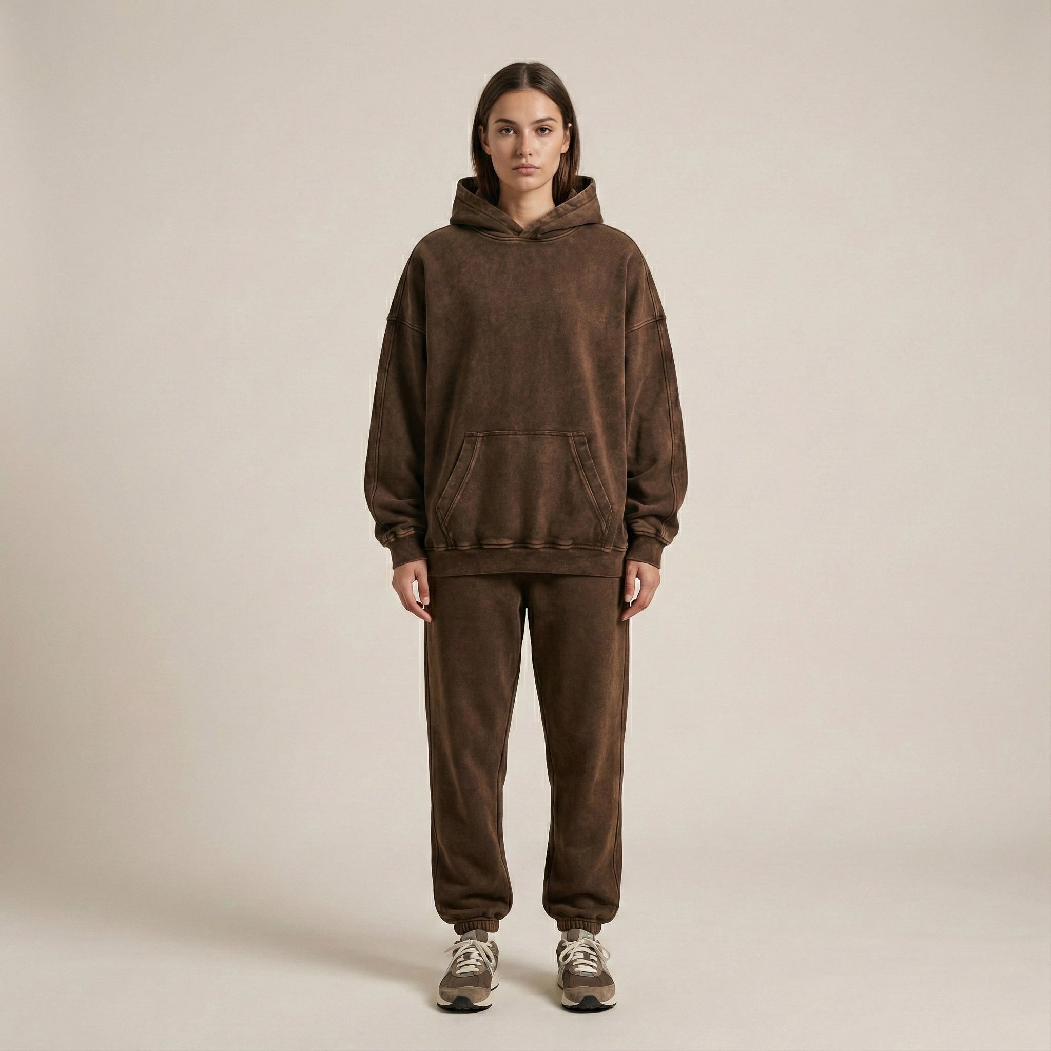 Person wearing a brown hoodie and pants set on a beige background