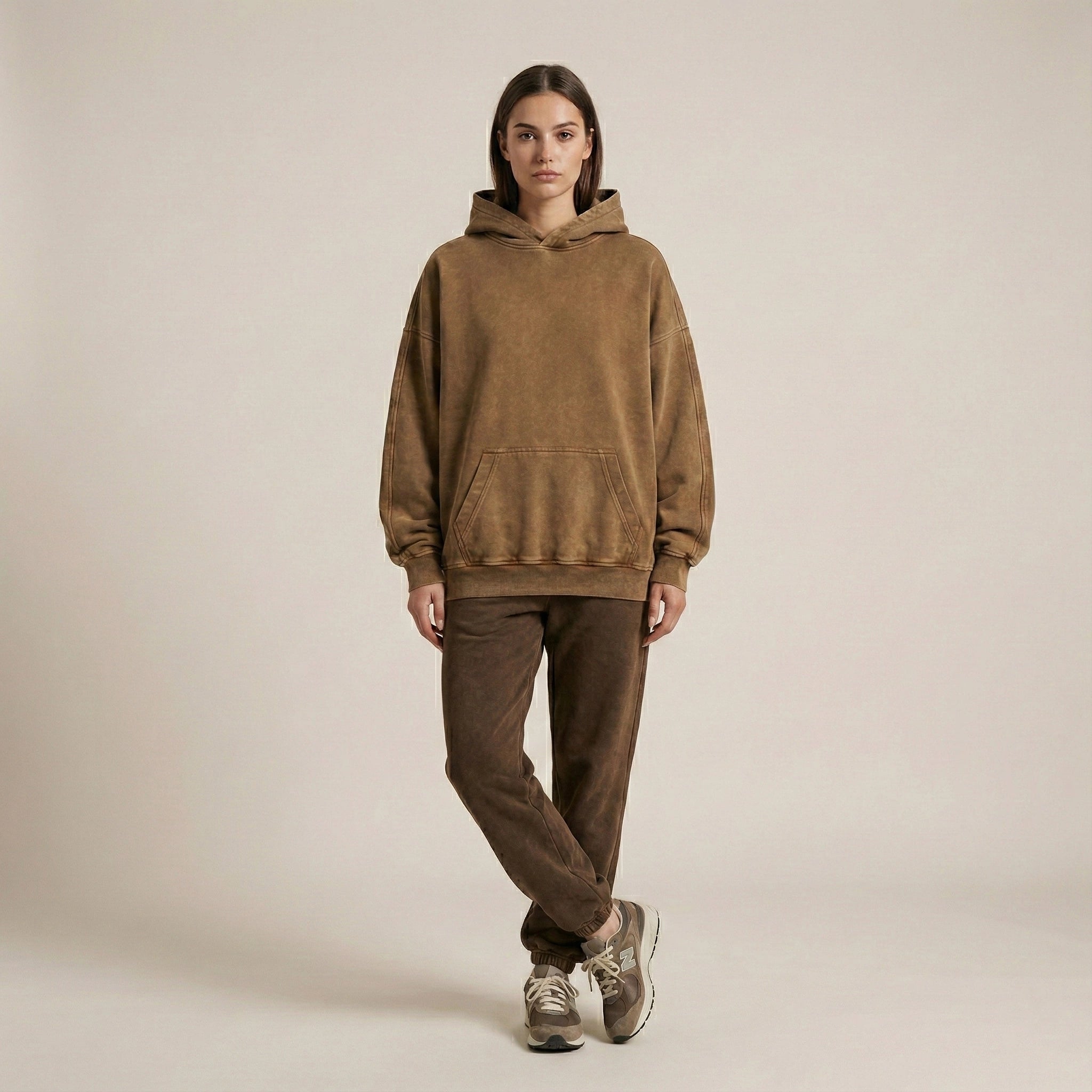 Person wearing a brown hoodie and pants on a beige background