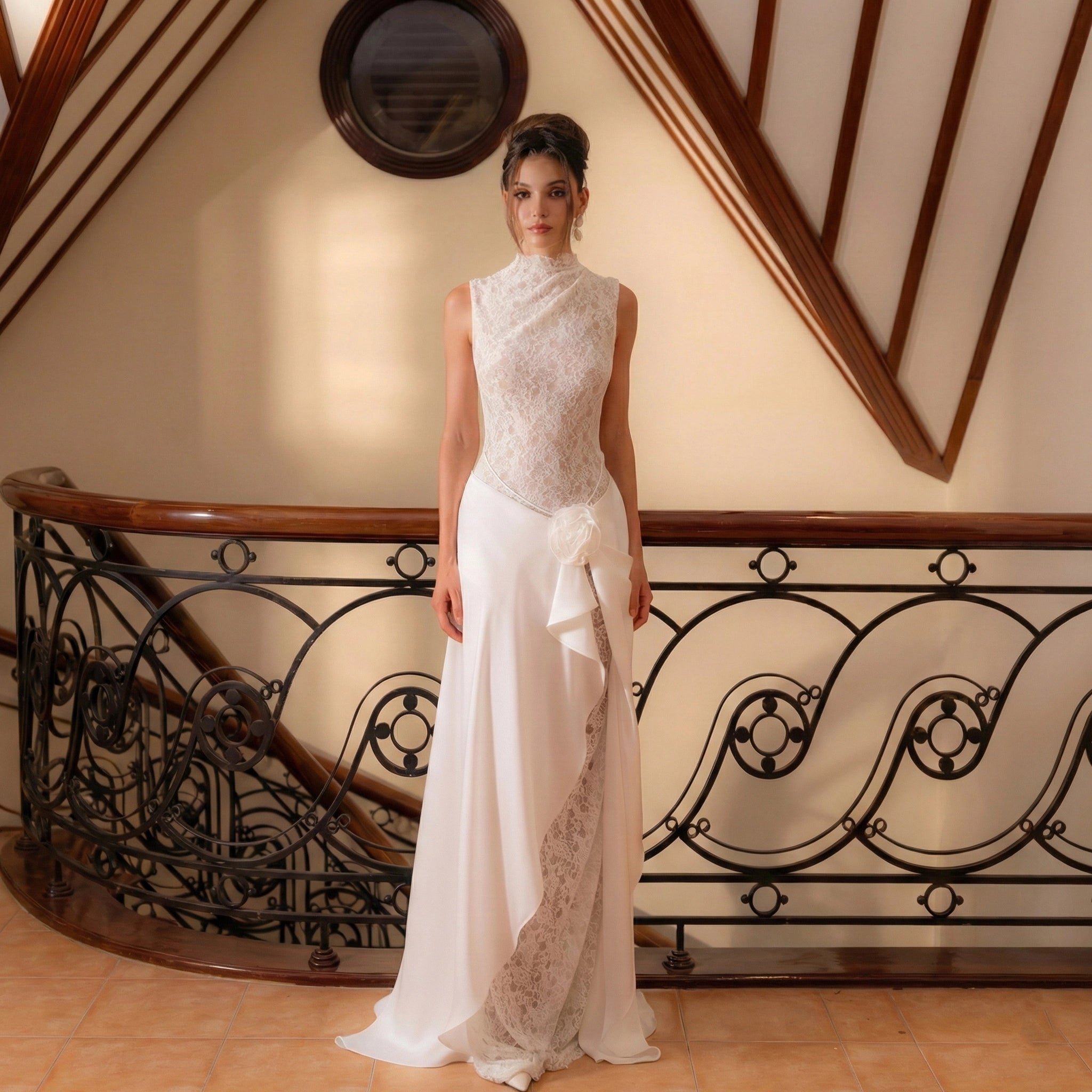 Woman in a white lace dress standing in front of an ornate staircase.