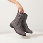 A pair of gray lace-up ankle boots with side zippers and low block heels, held by a person's hand against a clean off-white studio background.