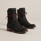 A pair of black suede ankle boots with dark burgundy laces, studded detailing on the collar, and low block heels, photographed on a neutral beige background.