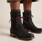 Black suede ankle boots with dark burgundy laces, studded detailing on the collar, and a low block heel, shown on a model against a light beige background.