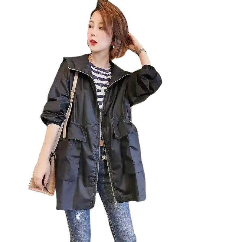 A woman modeling a black hooded jacket with a front zipper, worn over a striped shirt and blue jeans, against a plain white background.