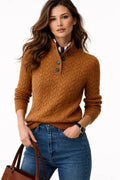 Woman wearing a brown cable knit sweater with a white shirt underneath, holding a brown handbag.