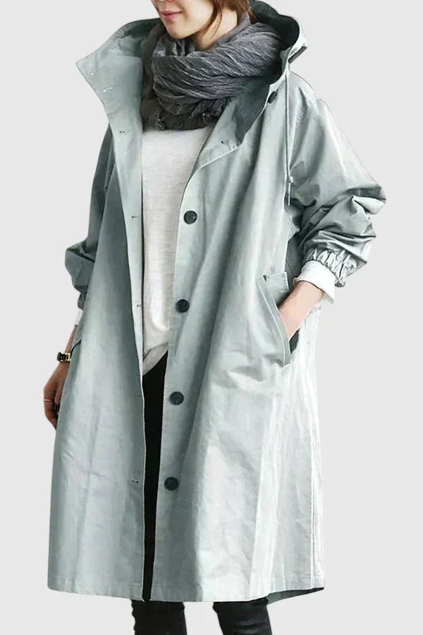 Person wearing a long light gray coat with a hood on a plain background