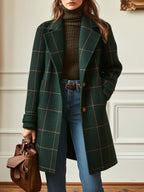 Person wearing a green plaid coat, brown sweater, and blue jeans, holding a brown leather bag.