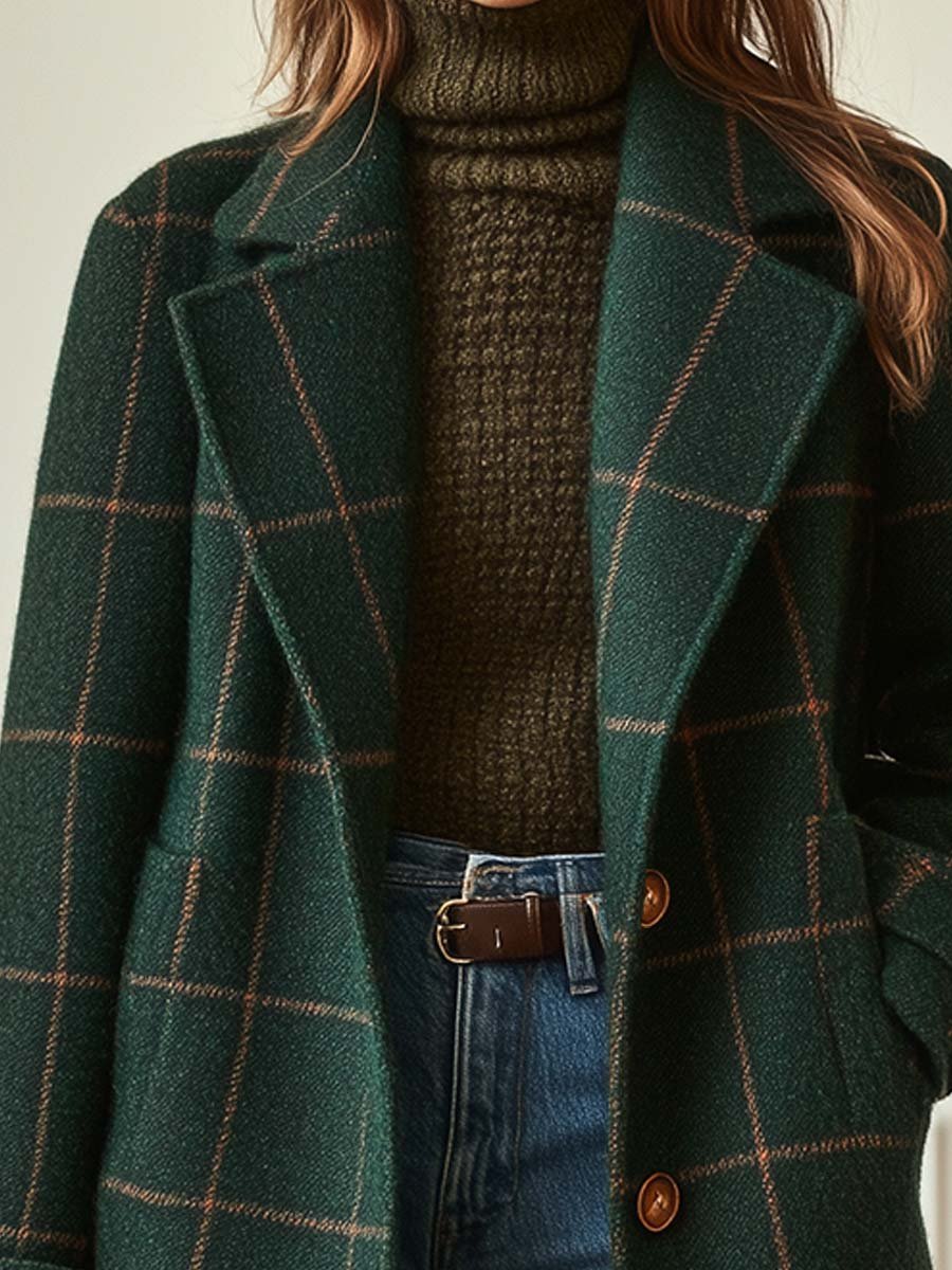 Green plaid coat with brown buttons worn over a brown sweater and blue jeans.