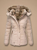 A women's puffer jacket in a light beige or cream color, featuring a plush brown faux-fur trimmed hood and a button-front closure, shown against a solid beige background.