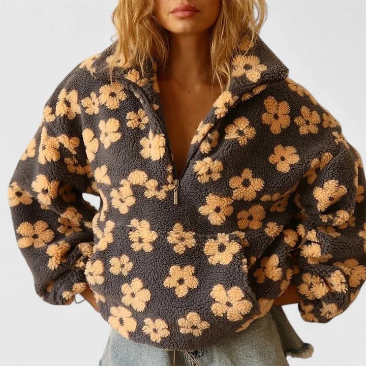 A woman wearing a dark gray fleece quarter-zip jacket with a tan floral pattern, paired with light-wash jeans against a plain white background.