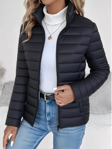 Person wearing a black puffer jacket over a white sweater and blue jeans on a neutral background