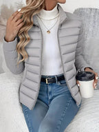 Person wearing a gray puffer jacket, white turtleneck, and blue jeans, holding a coffee cup.