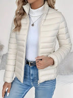 Person wearing a white puffer jacket over a light blue sweater and jeans on a neutral background