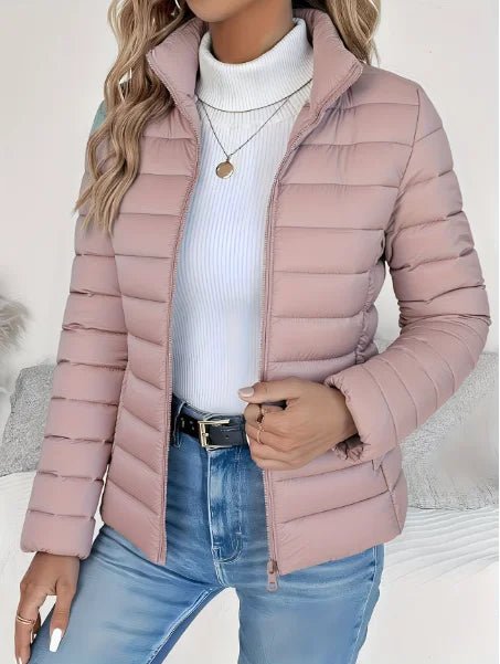 Person wearing a pink puffer jacket over a white turtleneck and blue jeans on a neutral background