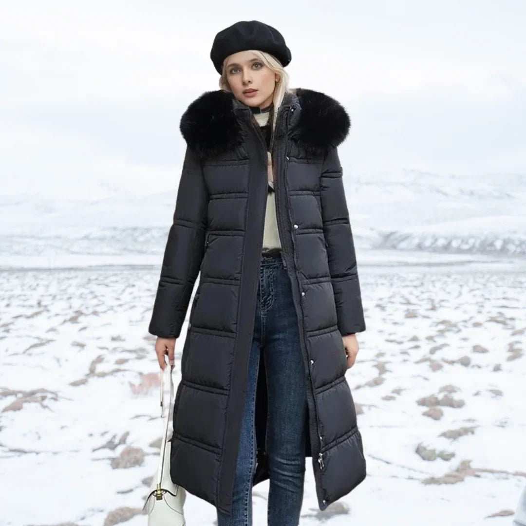 Woman wearing a long black puffer coat with a fur hood in a snowy landscape