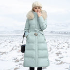 Woman wearing a long light blue puffer coat with a fur-lined hood in a snowy landscape.