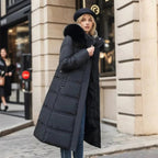 Woman wearing a long black puffer coat with fur hood on a city street.