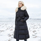 Woman wearing a long black puffer coat with a fur-lined hood in a snowy landscape.