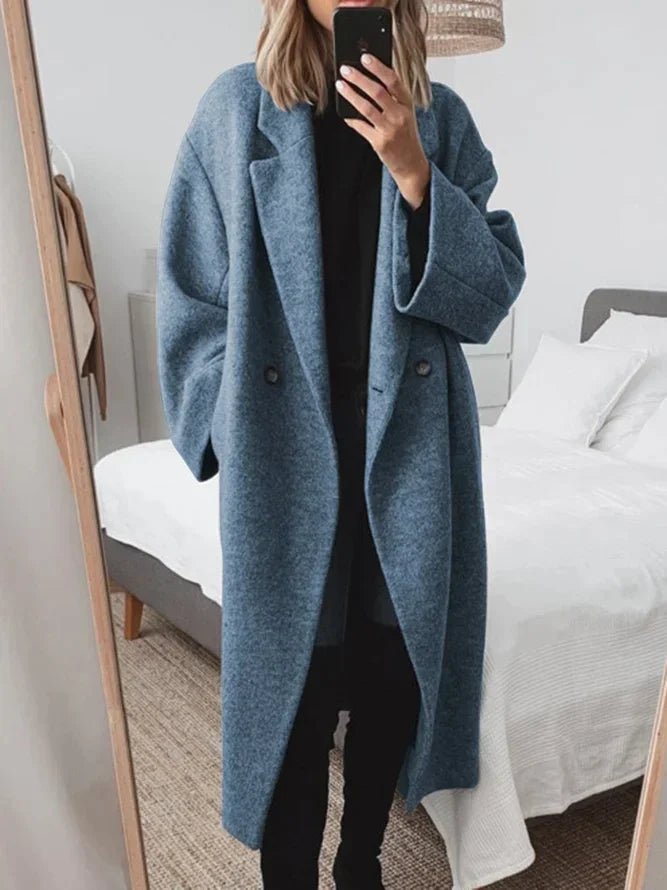 Person wearing a blue coat taking a mirror selfie in a bedroom.