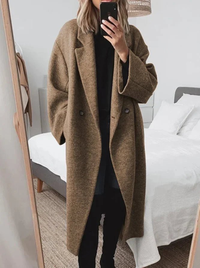 Person wearing a brown coat taking a mirror selfie in a bedroom.