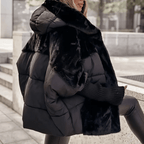 A woman wearing a black puffer jacket with a thick black faux fur collar and matching faux fur trim, photographed outdoors on stone steps.